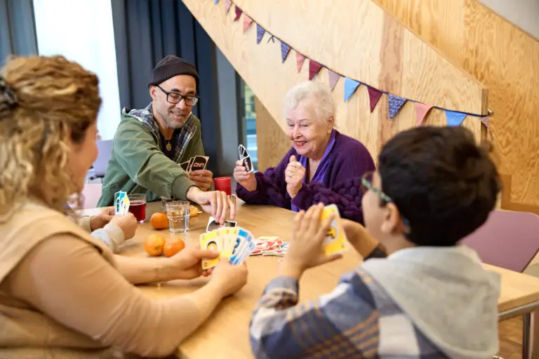 Menschen unterschiedlichen Alters sitzen gemeinsam an einem Tisch und spielen Karten